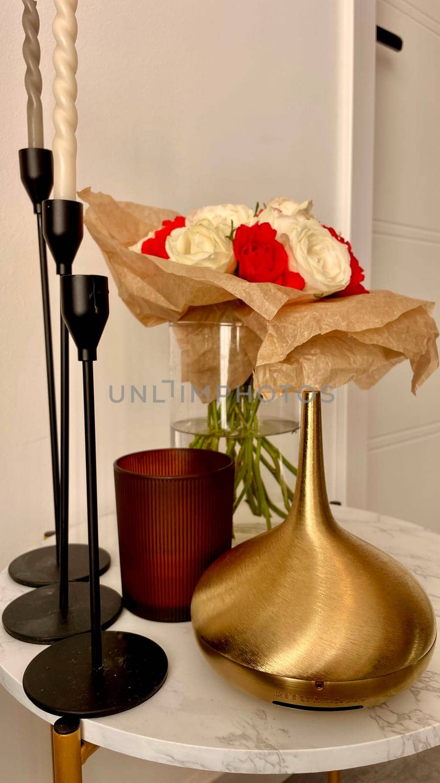 There are candlesticks, an aroma lamp, a candle and a bouquet of roses on a round table. High quality photo