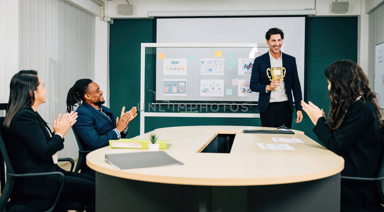 In a meeting room, a triumphant businessman holds an award trophy, surrounded by congratulatory teamwork. This exemplifies success, leadership, and achievement in business management.