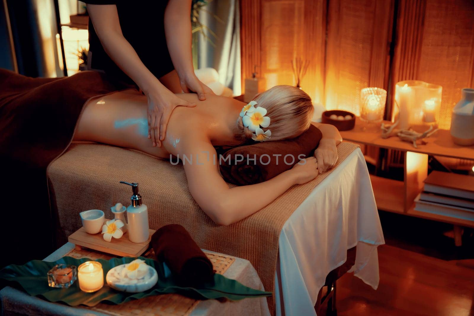 Caucasian woman customer enjoying relaxing anti-stress spa massage and pampering with beauty skin recreation leisure in warm candle lighting ambient salon spa at luxury resort or hotel. Quiescent