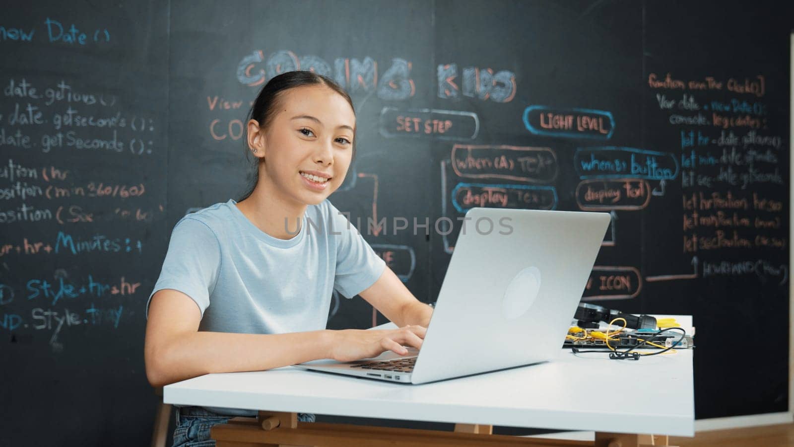 Smart girl programing system by using laptop at blackboard. Highschool student writing engineering code or prompt while looking at camera at STEM technology class. Creative education. Edification.