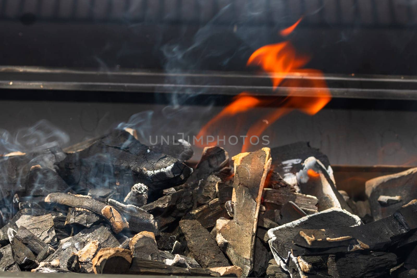 Barbecue grill pit with glowing and flaming hot open fire with red flame, hot charcoal briquettes and embers by vladispas