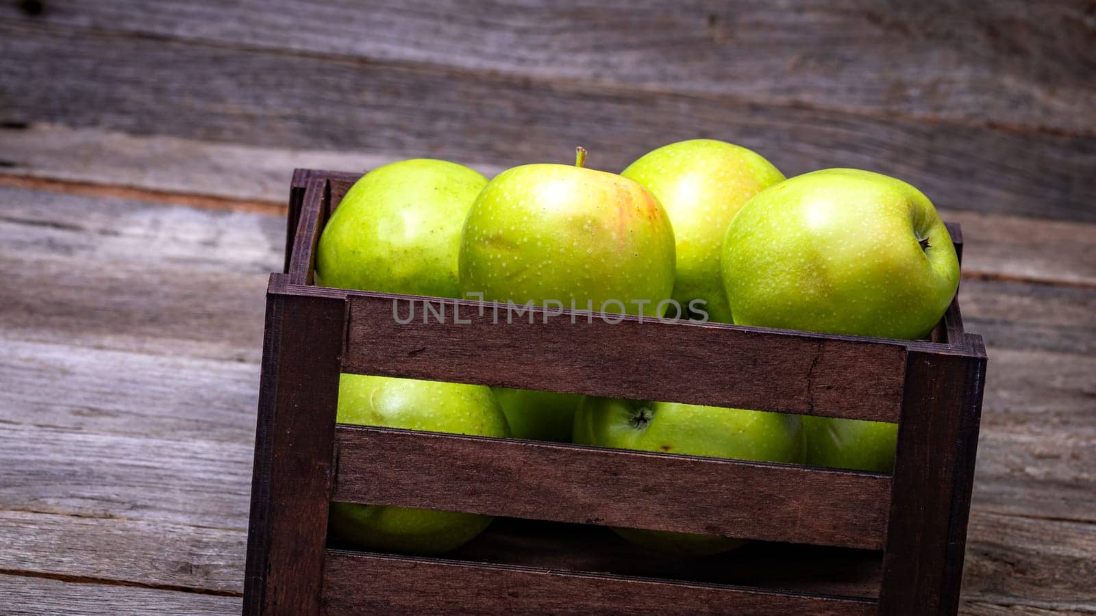 Wooden crate with ripe green apples on wooden table.