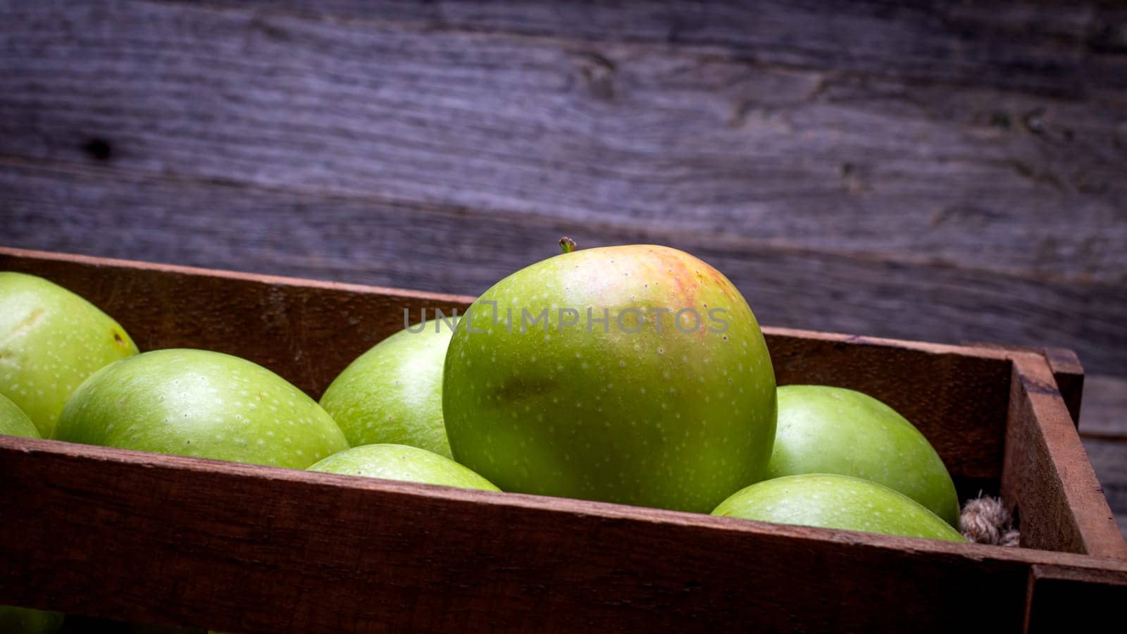 Wooden crate with ripe green apples on wooden table. by vladispas