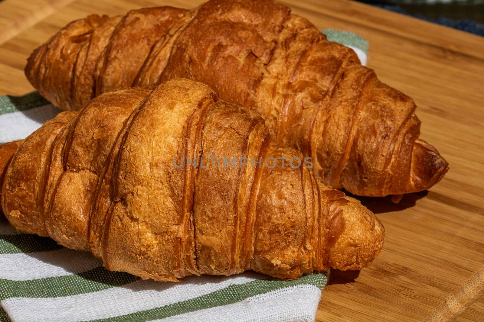 Detail of fresh croissant on wooden table. Food and breakfast concept. Close up photo of French buttery croissant  by vladispas