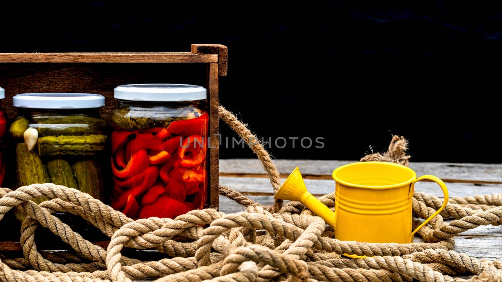 Wooden crate with glass jars with pickled red bell peppers and pickled cucumbers (pickles) isolated. Jars with variety of pickled vegetables. Preserved food concept in a rustic composition.