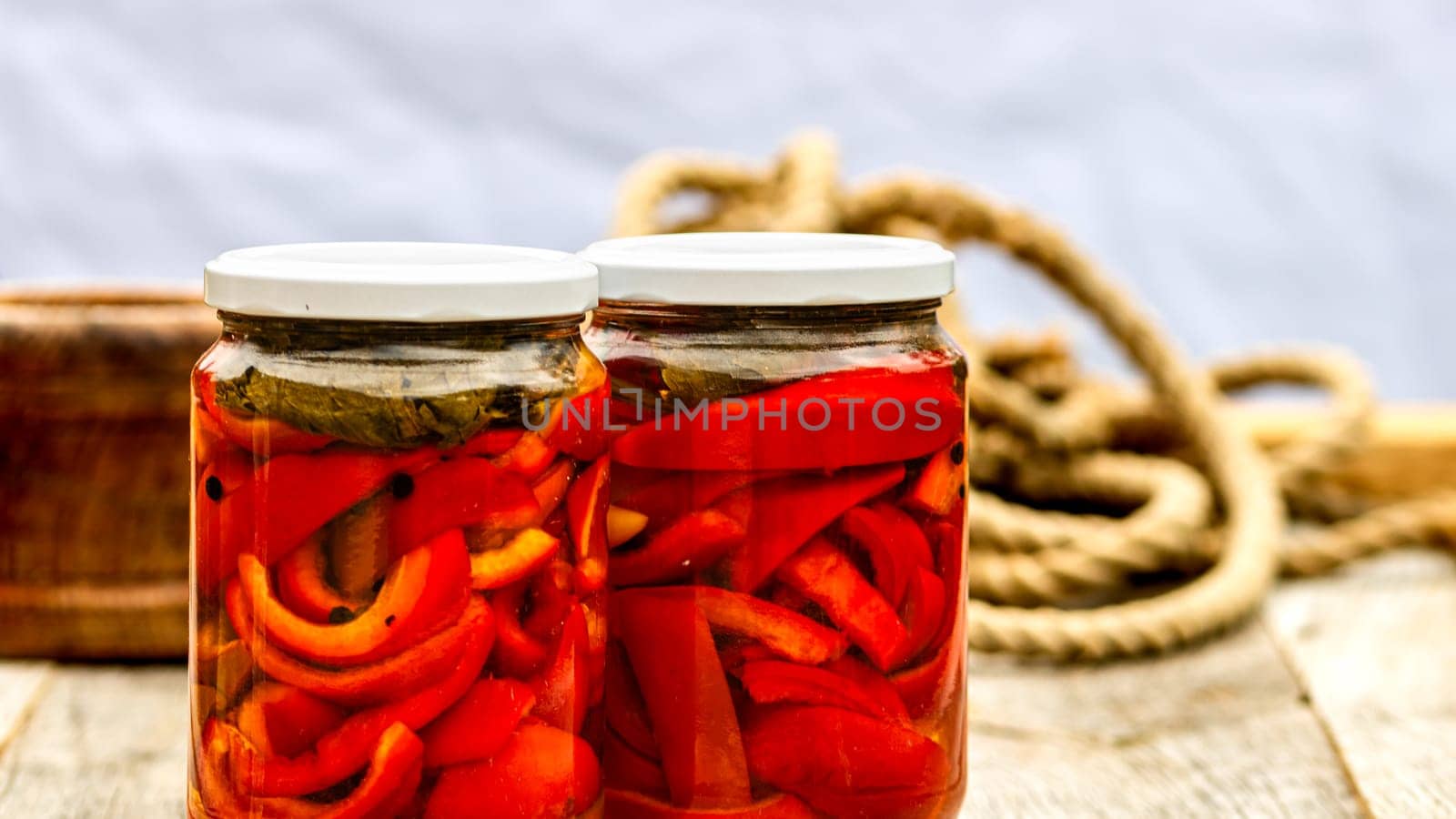 Glass jars with pickled red bell peppers.Preserved food concept, canned vegetables isolated in a rustic composition. by vladispas