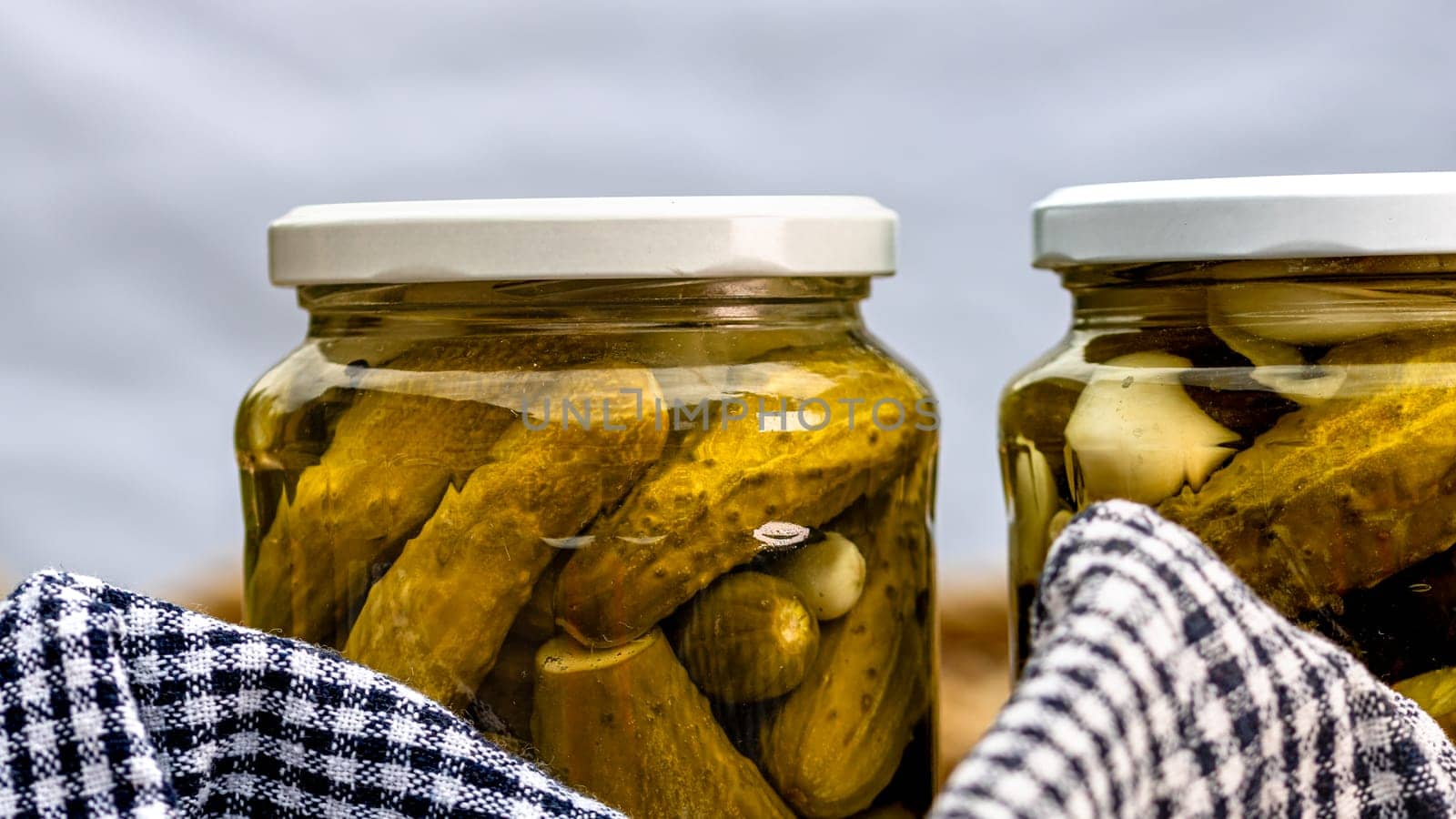 Glass jars with pickled red bell peppers and pickled cucumbers (pickles) isolated. Jars with variety of pickled vegetables. Preserved food concept in a rustic composition.