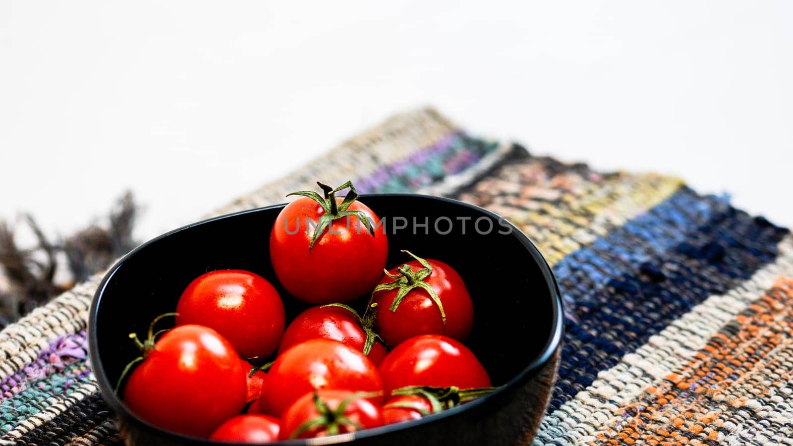 Detail of ripe cherry tomatoes in small black bowl on a rustic napkin. Ingredients and food concept