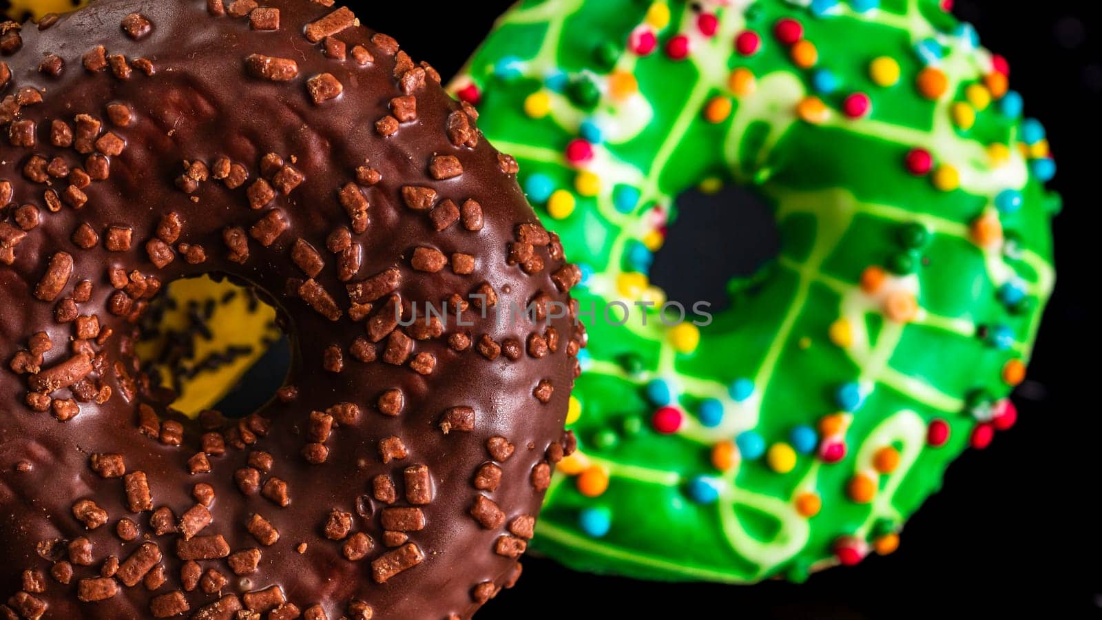 Fresh tasty colored donuts with sprinkles on black background