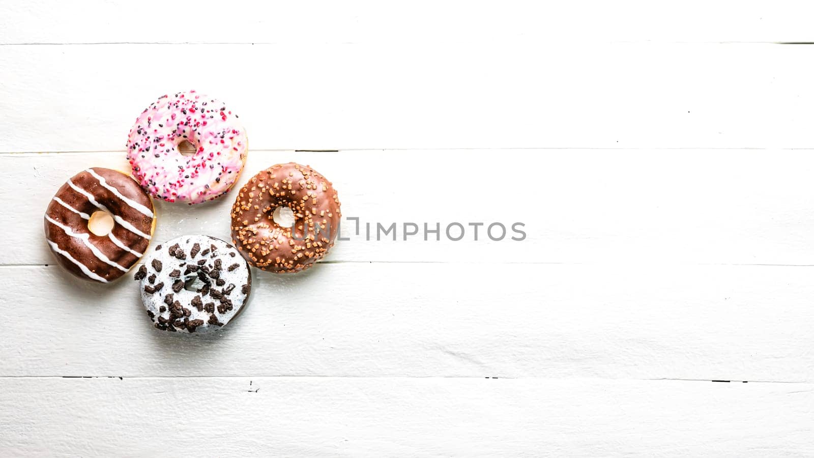 Colorful donuts on white wooden table. Sweet icing sugar food with glazed sprinkles, doughnut with frosting. Top view with copy space by vladispas