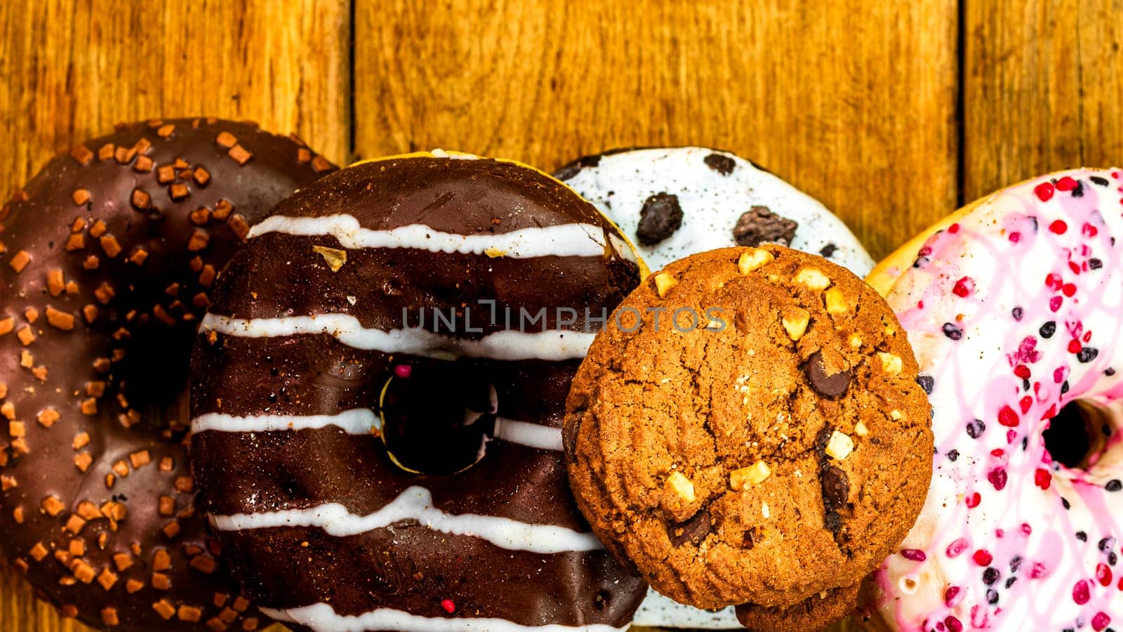 Colorful donuts on wooden table. Sweet icing sugar food with glazed sprinkles, doughnut with chocolate frosting. Top view with copy space