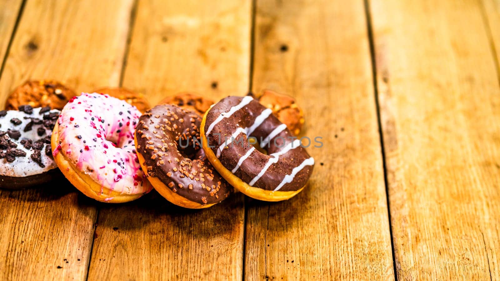 Colorful donuts on wooden table. Sweet icing sugar food with glazed sprinkles, doughnut with chocolate frosting. Top view with copy space