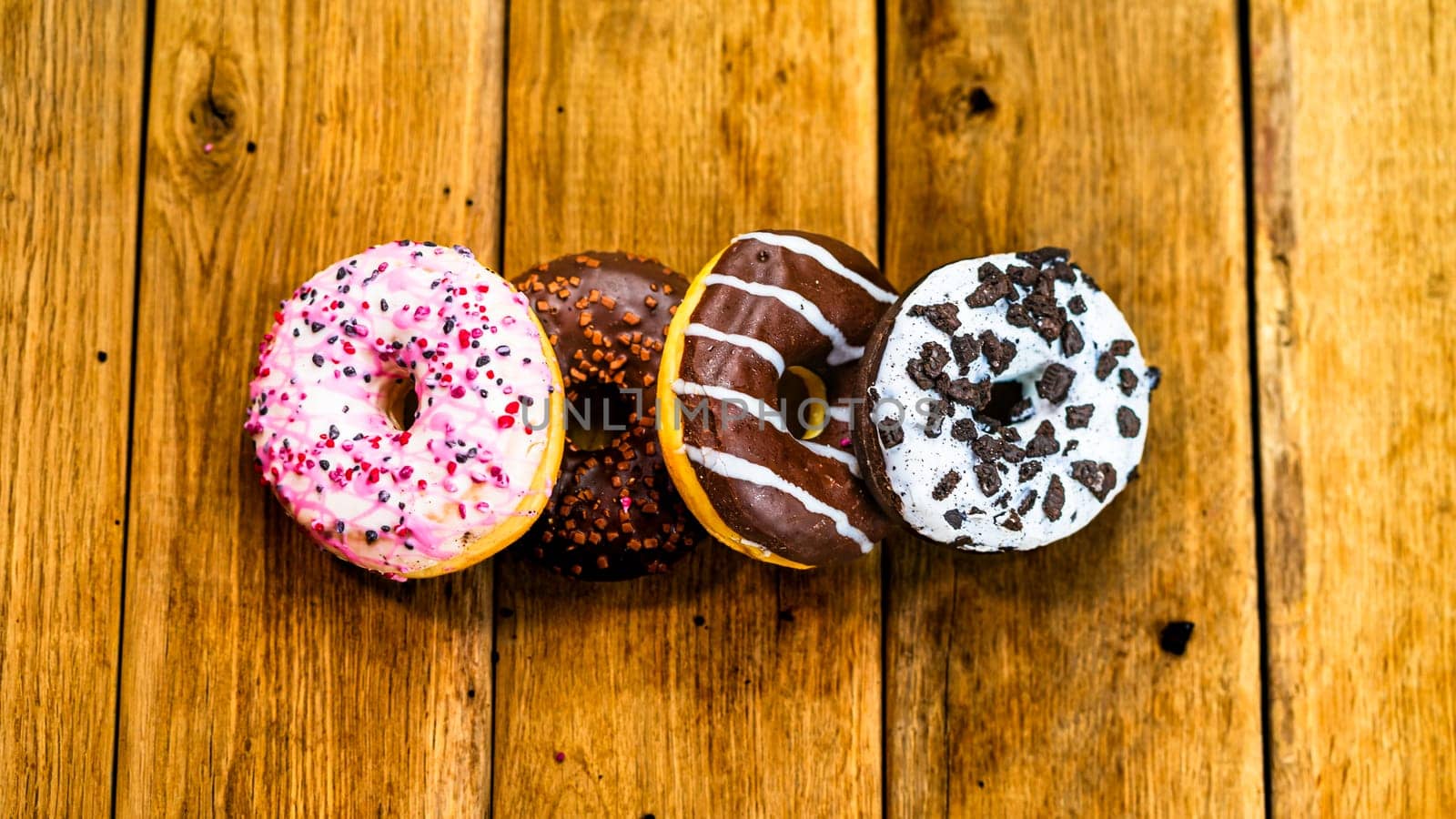 Colorful donuts on wooden table. Sweet icing sugar food with glazed sprinkles, doughnut with chocolate frosting. Top view with copy space