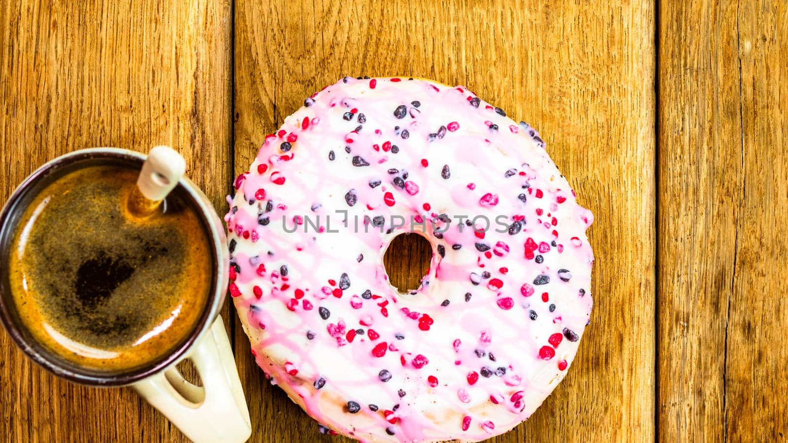 Colorful donuts and coffee cup on white wooden table. Sweet bakery with glazed sprinkles, breakfast concept. Top view with copy space by vladispas