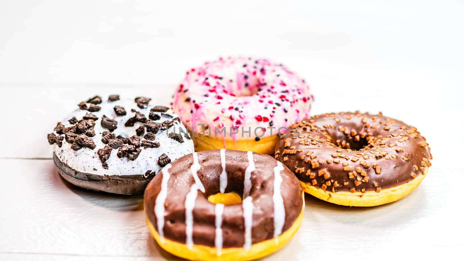 Colorful donuts on white wooden table. Sweet icing sugar food with glazed sprinkles, doughnut with frosting. Top view with copy space