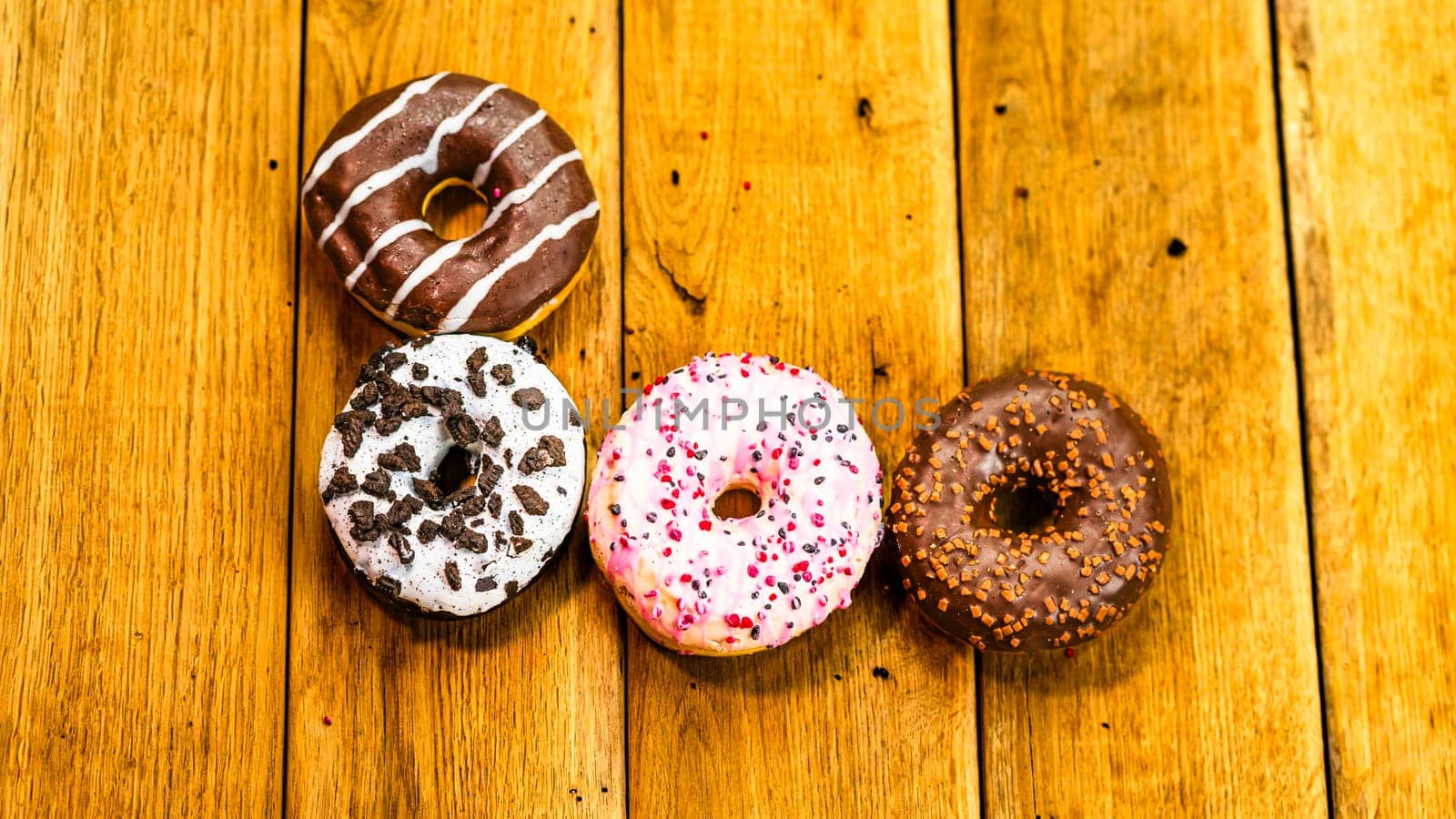 Colorful donuts on wooden table. Sweet icing sugar food with glazed sprinkles, doughnut with chocolate frosting. Top view with copy space