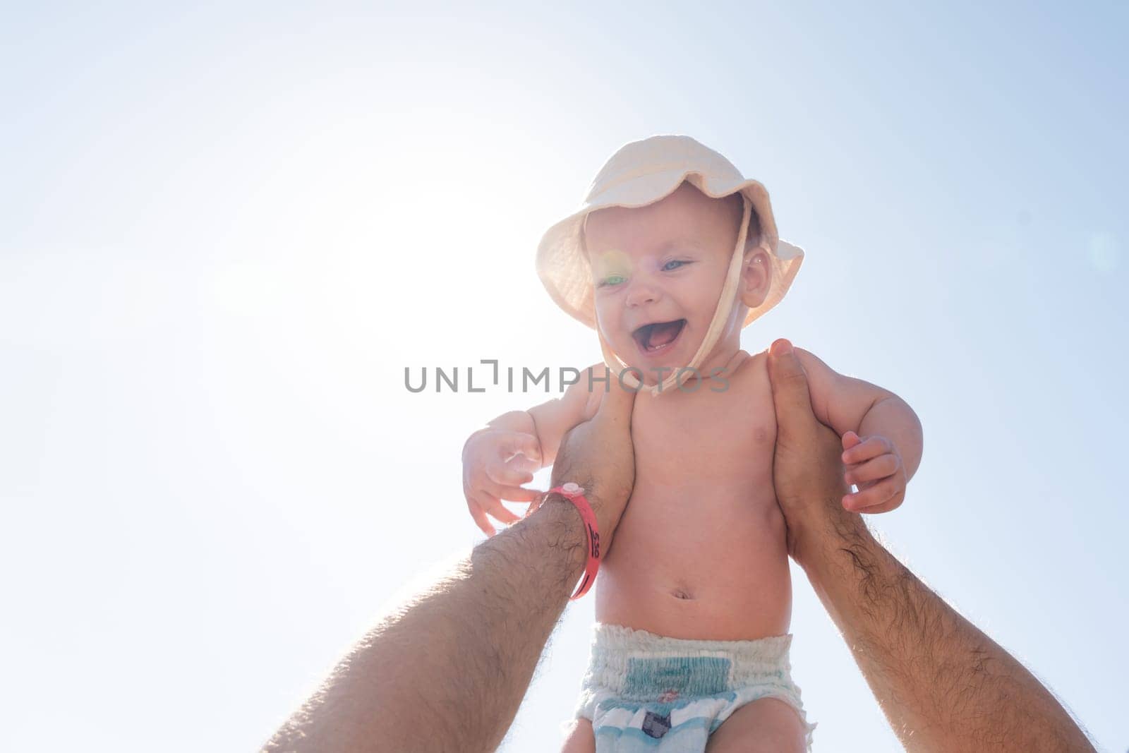 Father's hand lifts a joyful baby against a sunlit sky. Concept of paternal love and playful moments by Mariakray