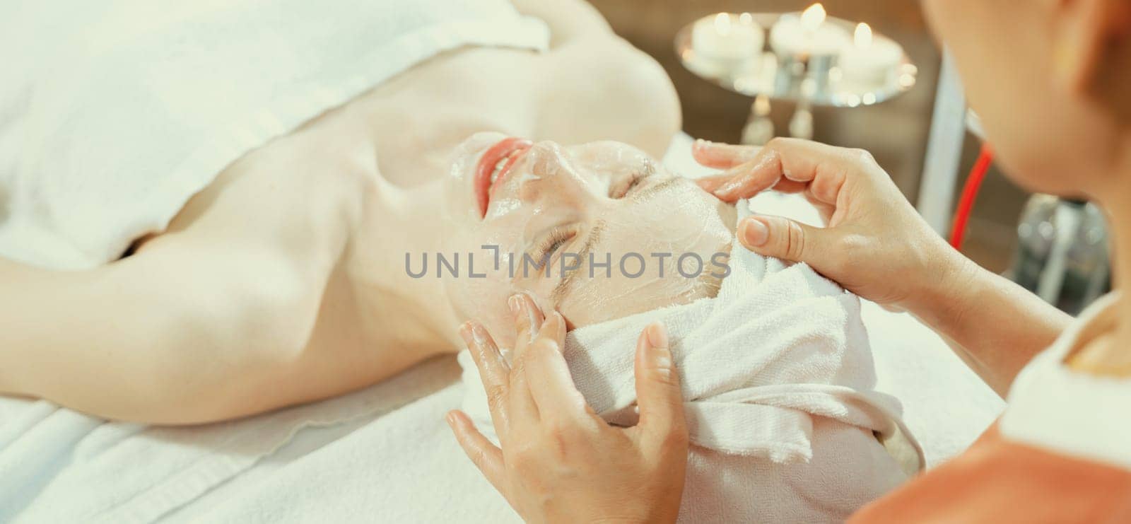 Portrait of beautiful caucasian woman having facial massage with homemade facial mask while lies on spa bed surrounded by beauty electrical equipment and peaceful nature environment. Tranquility.