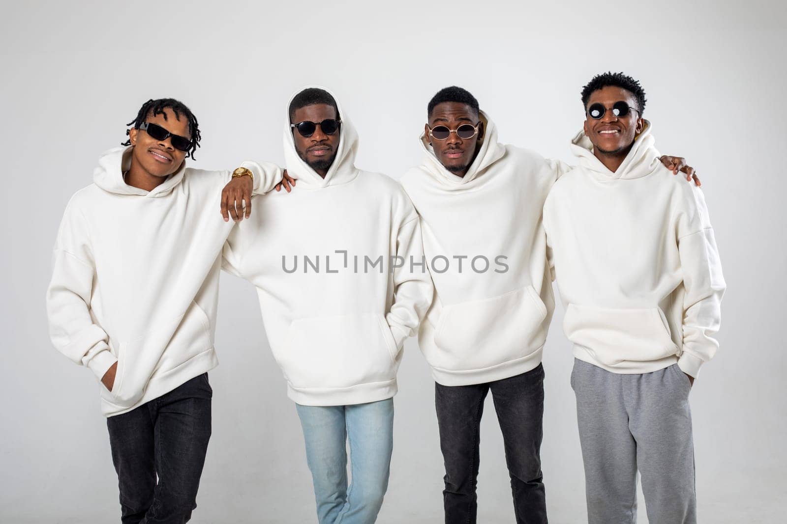 Group of African American guys in brown hoodies posing on a white background wearing sunglasses. High quality photo