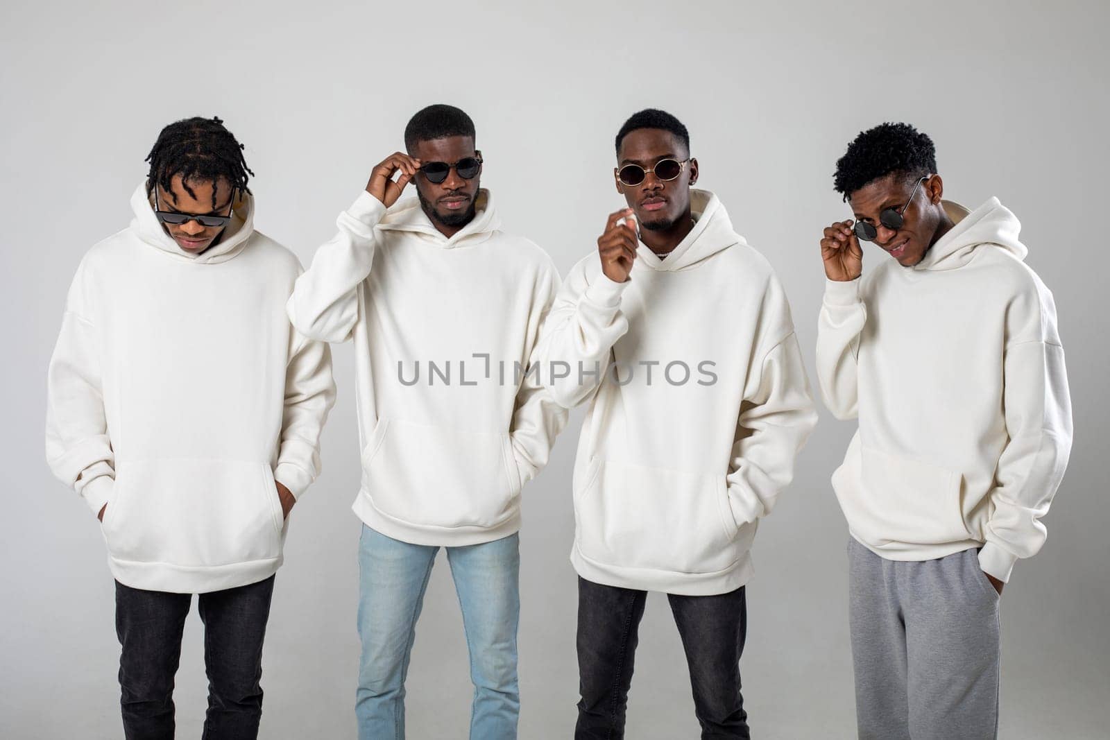 Group of African American guys in brown hoodies posing on a white background wearing sunglasses. High quality photo