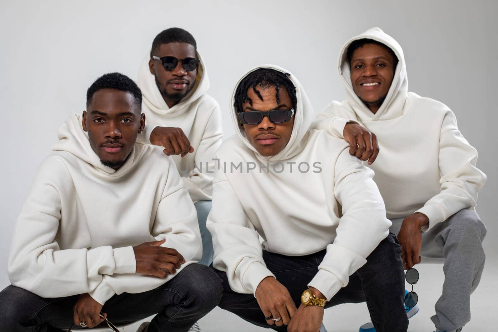 Group of African American guys in brown hoodies posing on a white background. Two in sunglasses. by Freeman_Studio