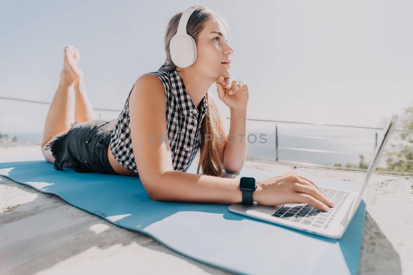 Digital nomad, Business woman working on laptop by the sea. Pretty lady typing on computer by the sea at sunset, makes a business transaction online from a distance. Freelance, remote work on vacation