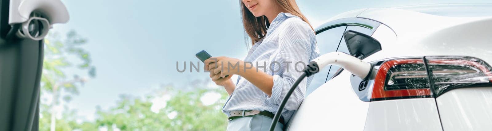 Young woman using smartphone to pay for electric car charging. Exalt by biancoblue