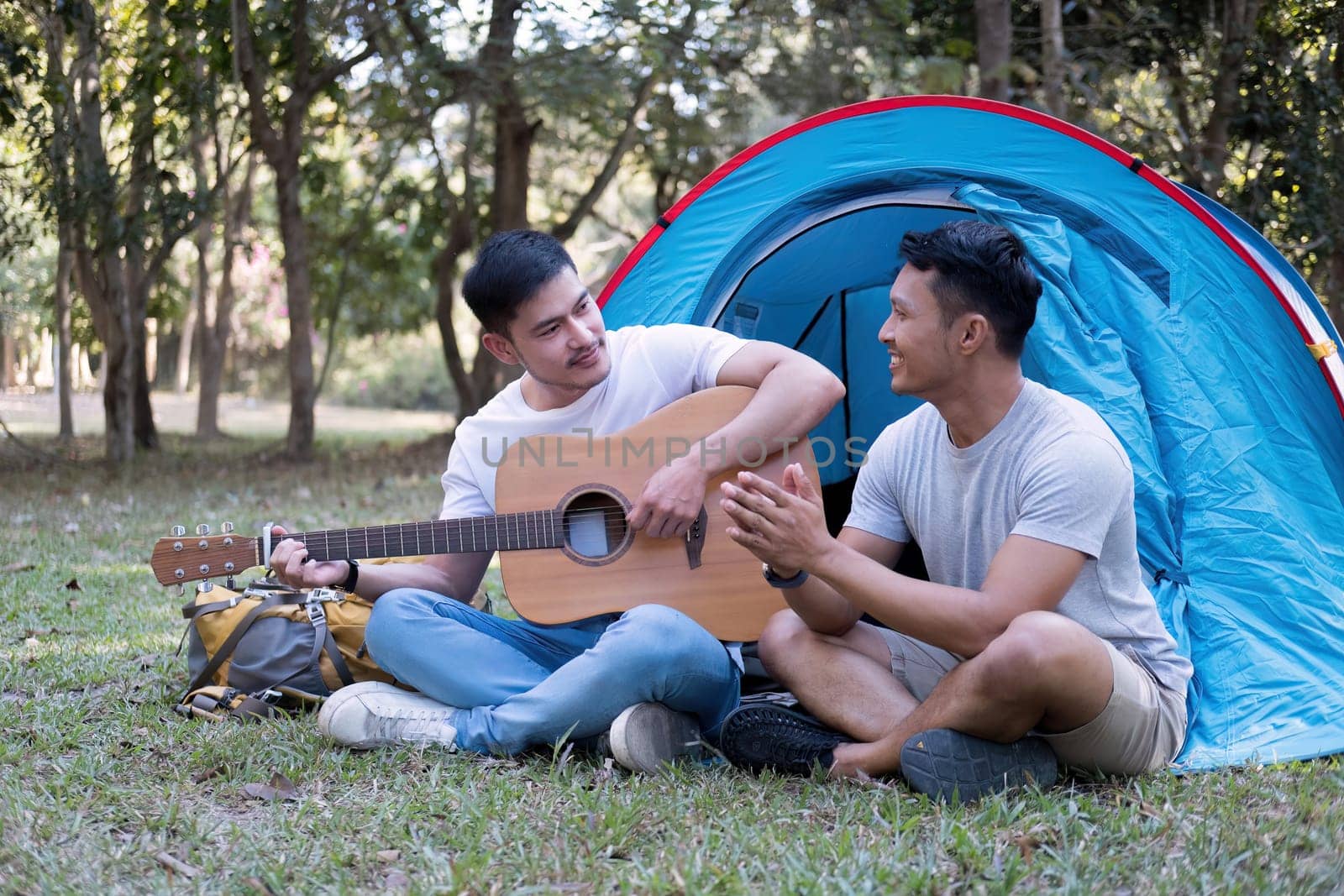 Asian LGBTQ couple enjoying nature, camping with tents in the forest area by the river, playing guitar..