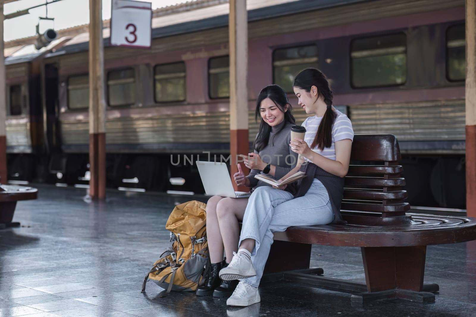 Two Asian female tourist friends are at the train station. Waiting for the train to travel to the provinces together on the weekend..