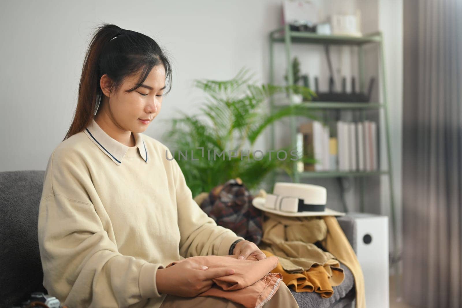 Smiling young woman sitting in living room packing bags and preparing things for vacations trip.