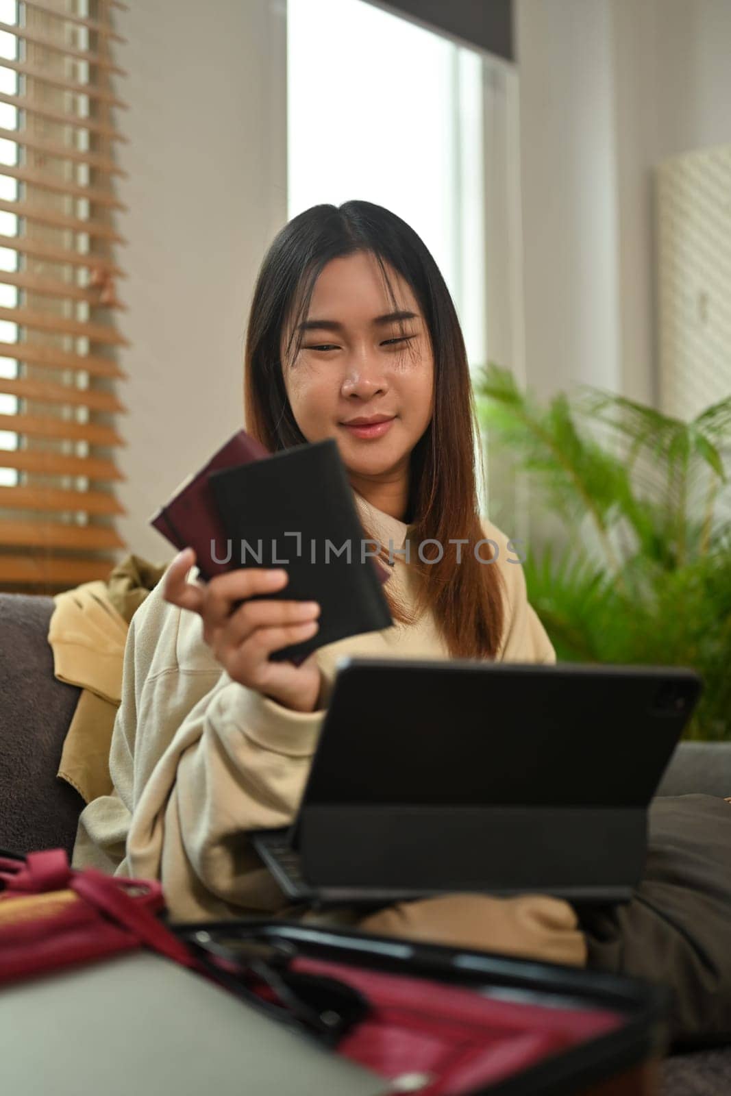 Pleasant young woman holding passport and booking flight tickets on digital tablet.