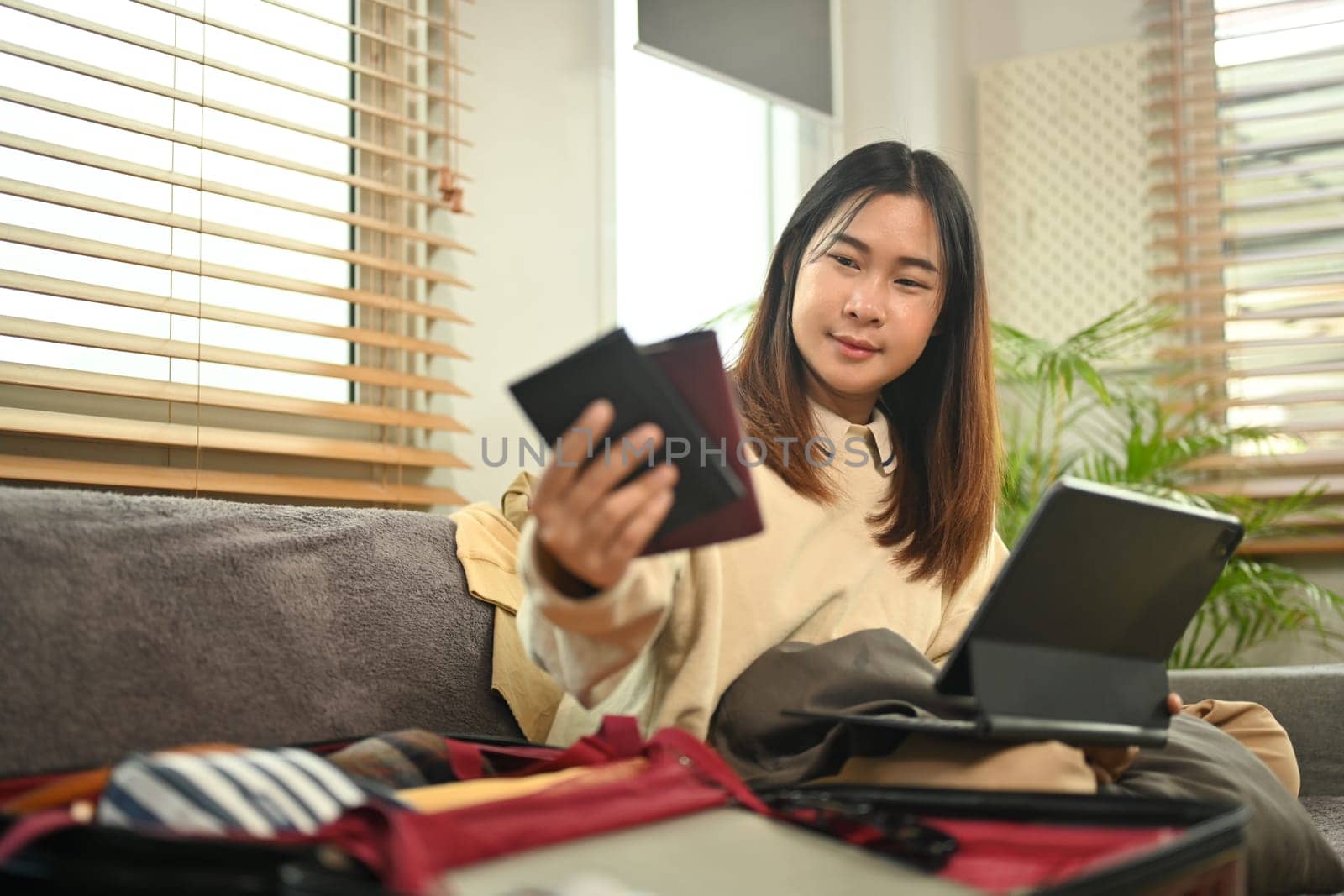 Smiling young woman holding passport and searching information weekend vacation trip on digital tablet.