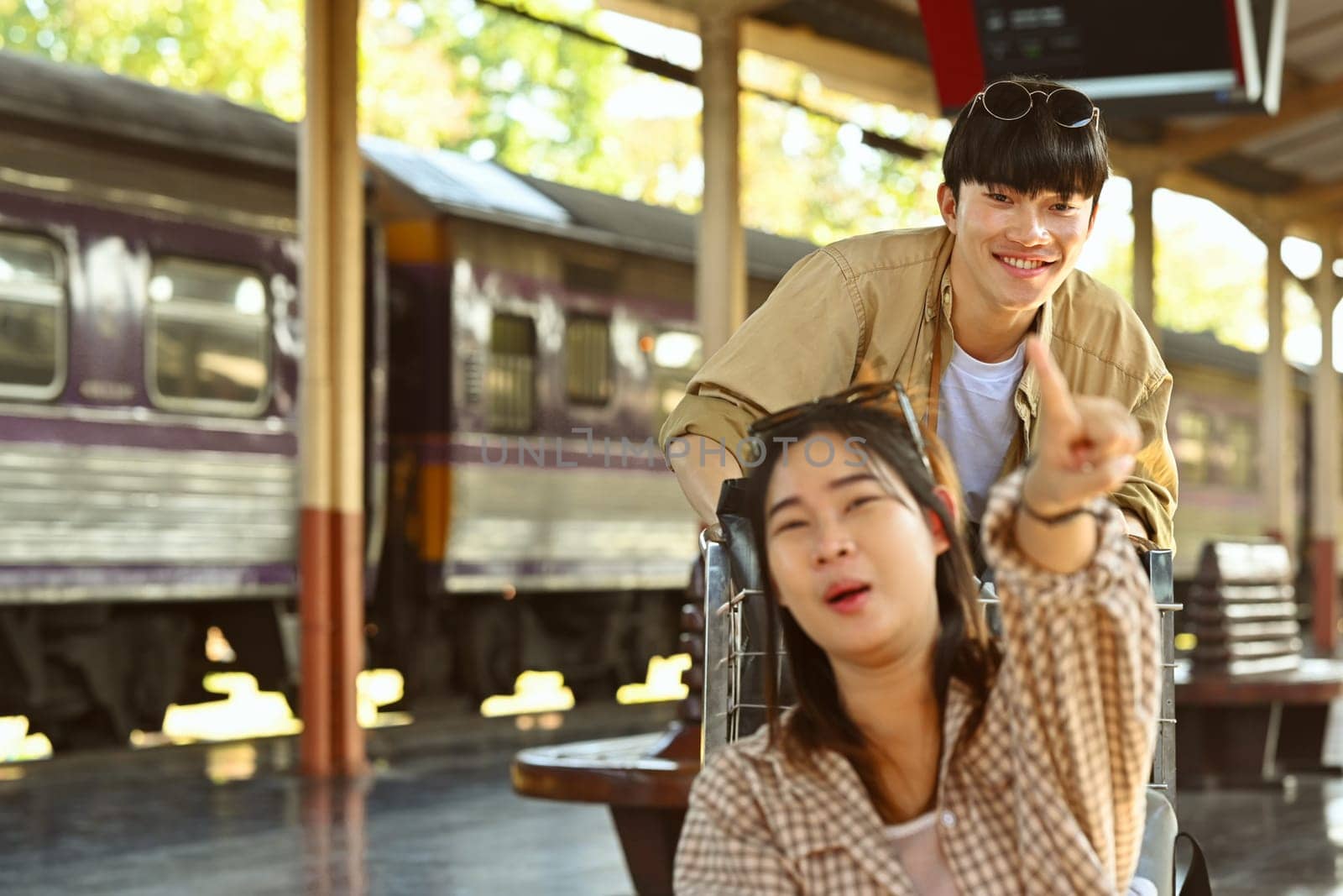 Ready to travel. Cheerful young couple waiting for train on railway station platform. Travel and lifestyle concept by prathanchorruangsak