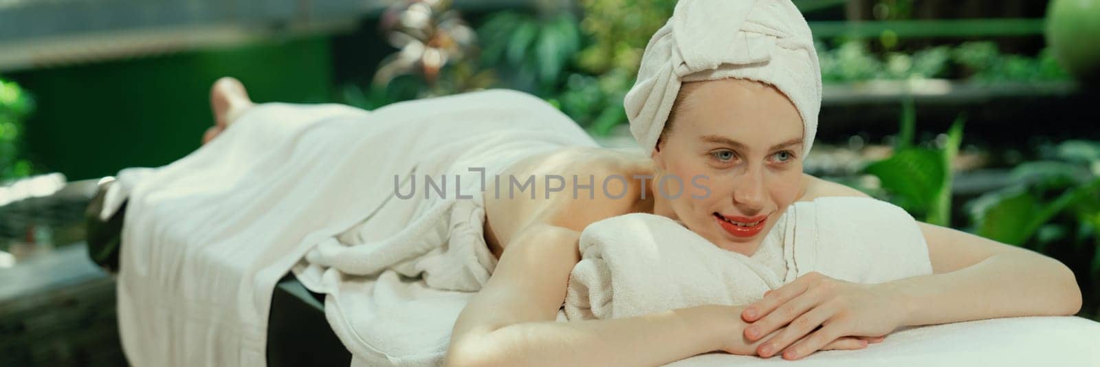 Beautiful young woman relaxes on a spa bed surrounded by nature. ready for a body massage. Attractive female in white towel lying peacefully during waiting for body massage. Close up. Tranquility