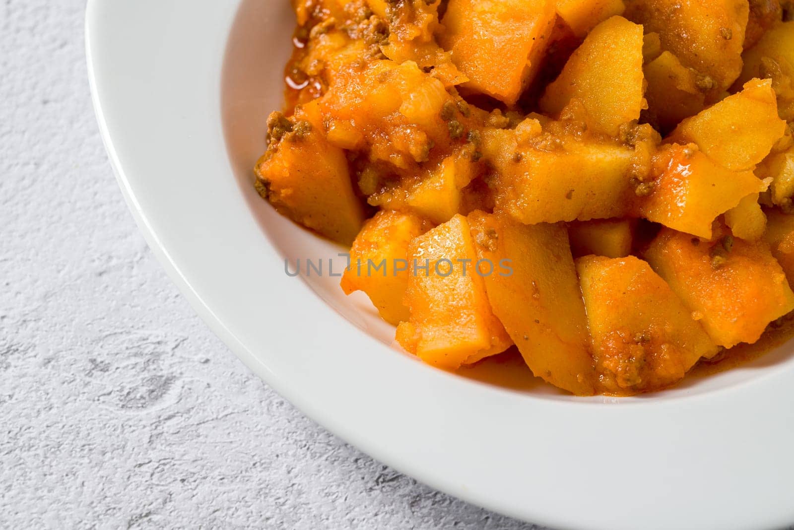 Minced meat and potato dish on white porcelain plate on stone table
