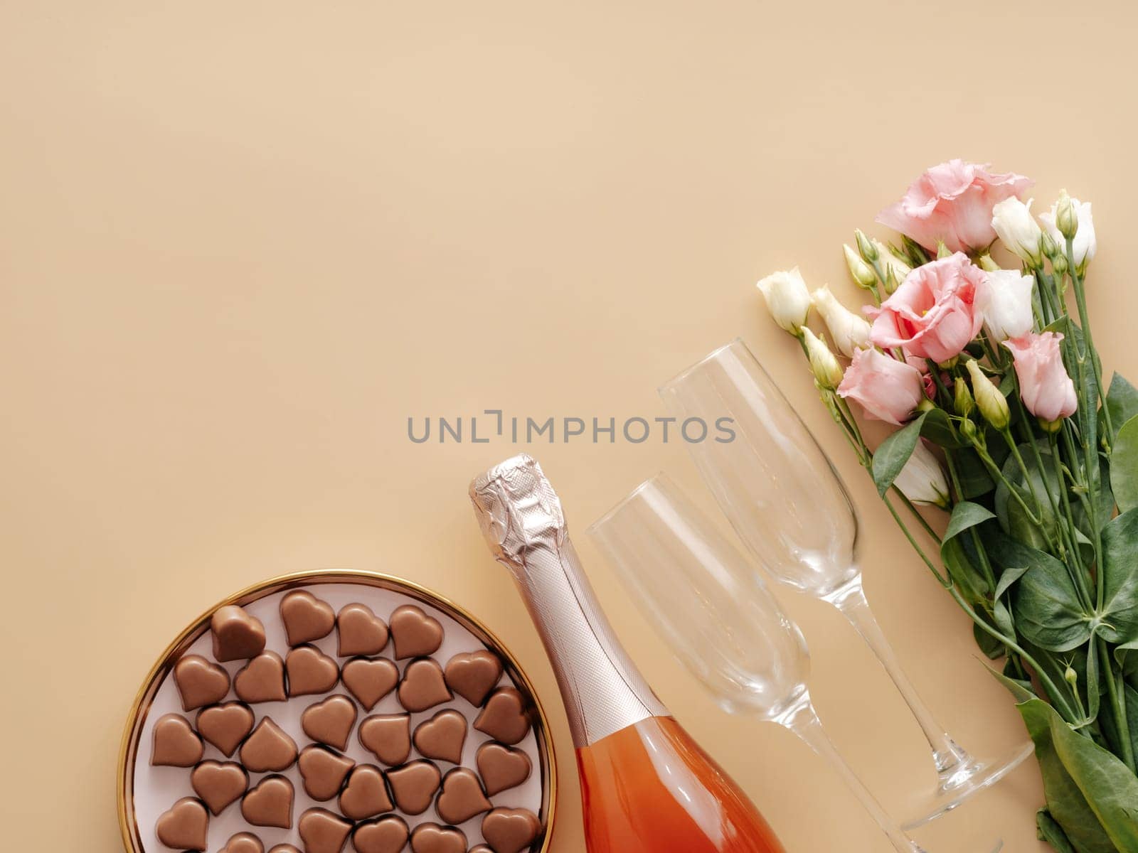 Valentines Day concept on pastel yellow background. Pink champagne bottle,glasses,flowers bouqet and romantic chocolate confections in heart shapes.Copyspace.Champagne beige background.Topview flatlay