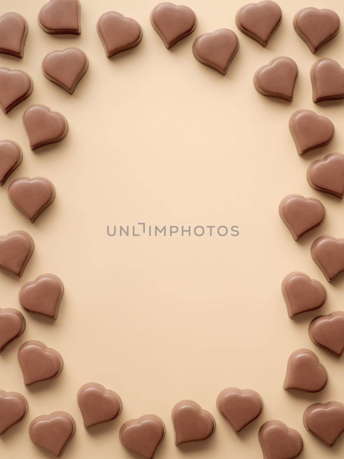Frame of romantic chocolate confections in heart shapes on pastel yellow background. Canvas with heart chocolate sweets on champagne beige background. Copy space. Valentines day background. Vertical