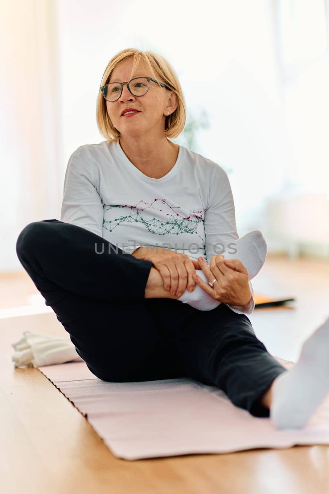 In a sunlit space, a senior woman gracefully practices rejuvenating yoga, focusing on neck, back, and leg stretches, embodying serenity and well-being by dotshock