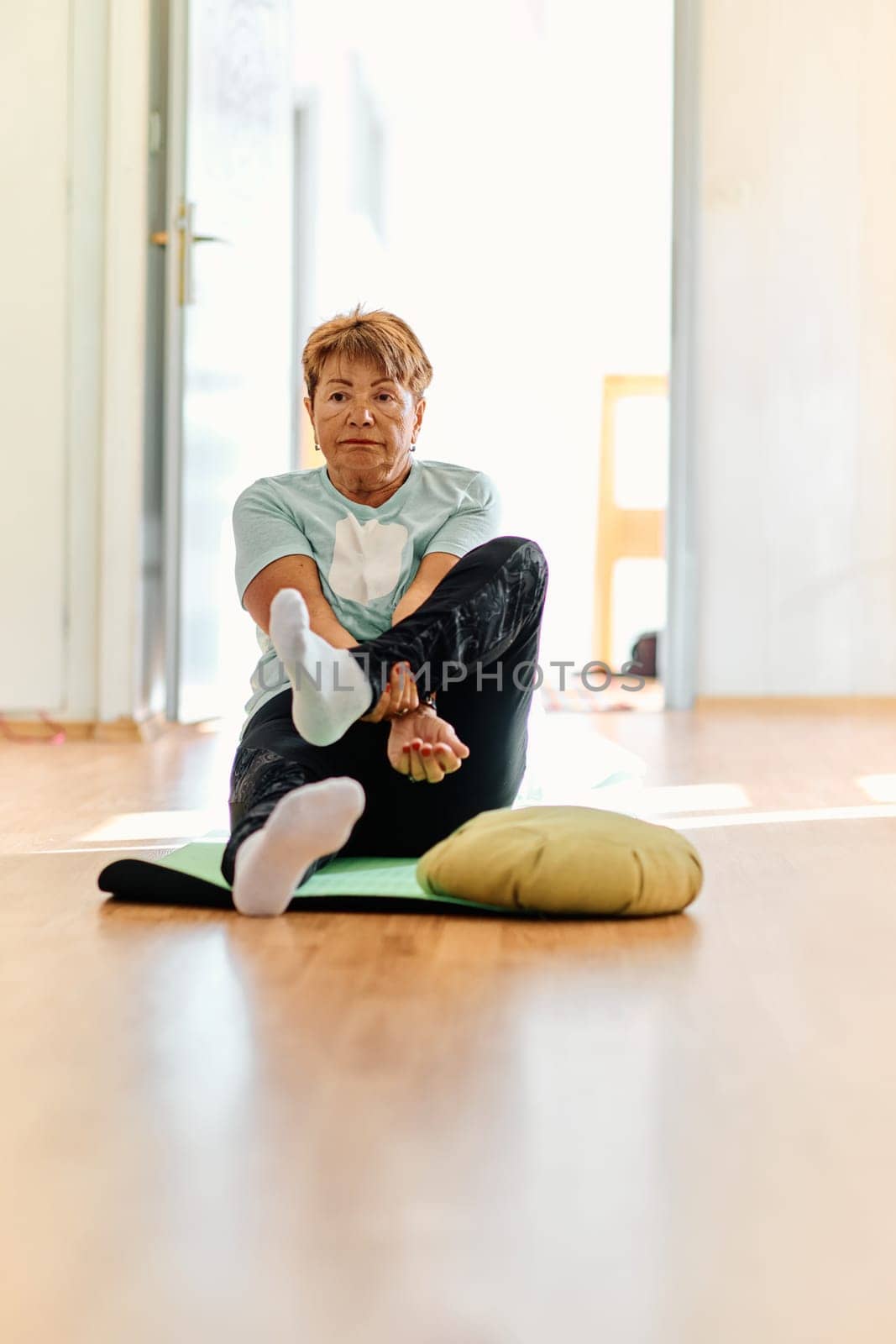 In a sunlit space, a senior woman gracefully practices rejuvenating yoga, focusing on neck, back, and leg stretches, embodying serenity and well-being.