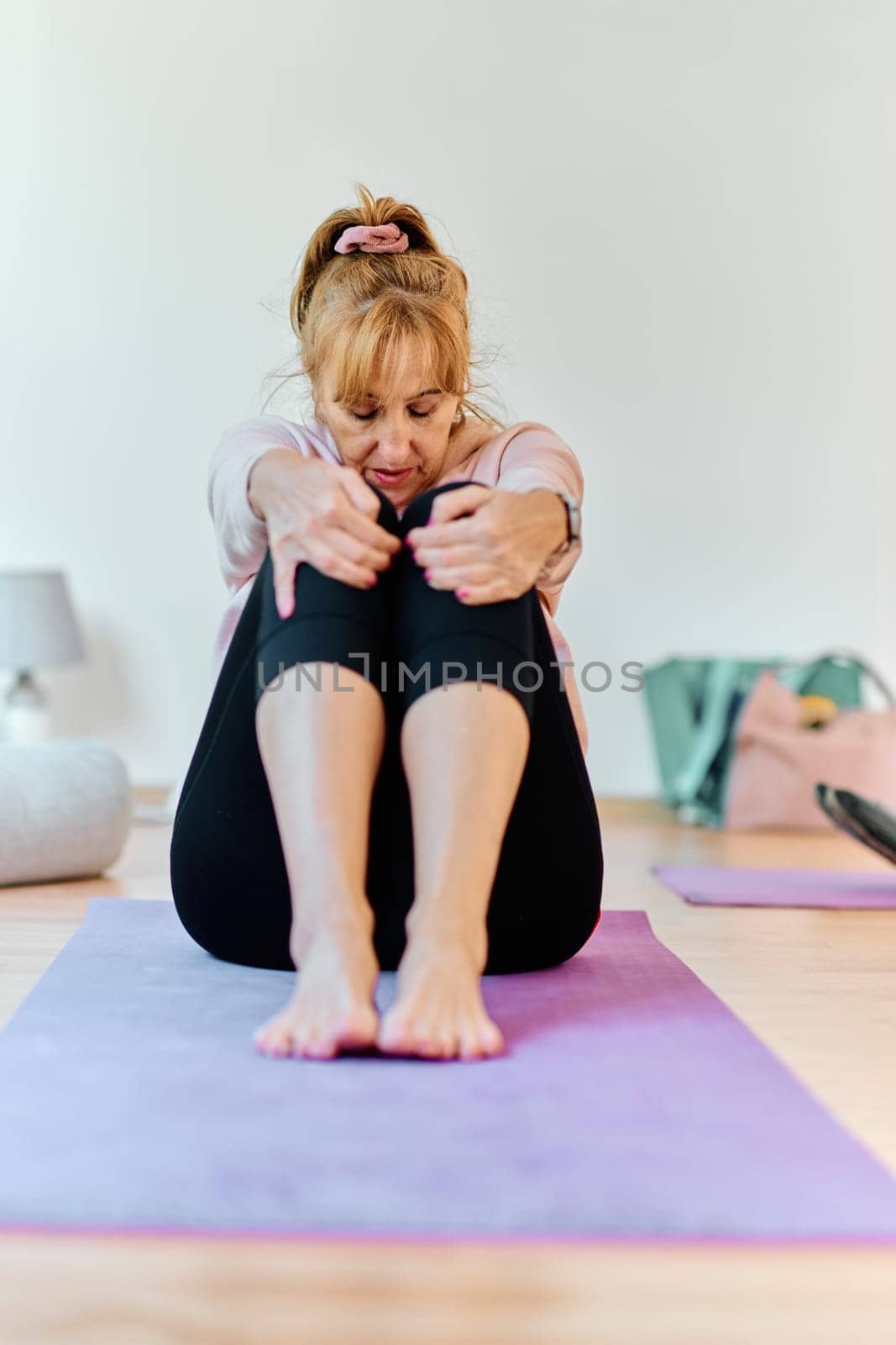 In a sunlit space, a senior woman gracefully practices rejuvenating yoga, focusing on neck, back, and leg stretches, embodying serenity and well-being by dotshock