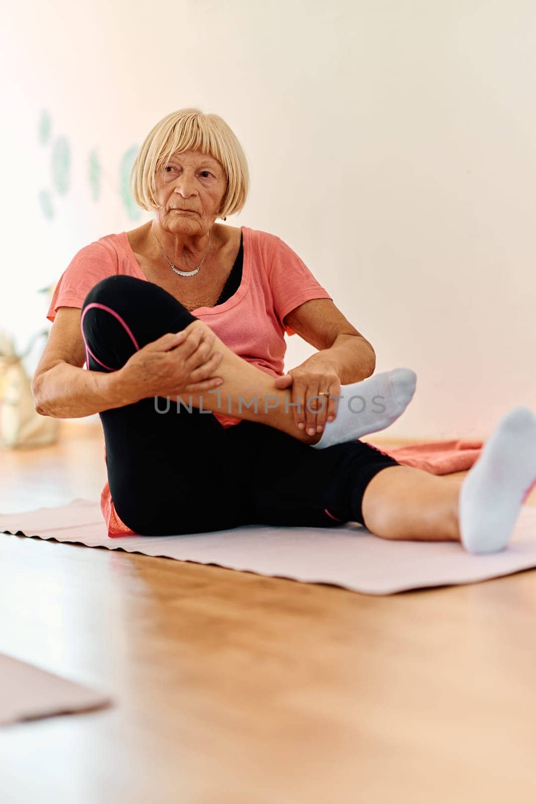 In a sunlit space, a senior woman gracefully practices rejuvenating yoga, focusing on neck, back, and leg stretches, embodying serenity and well-being.