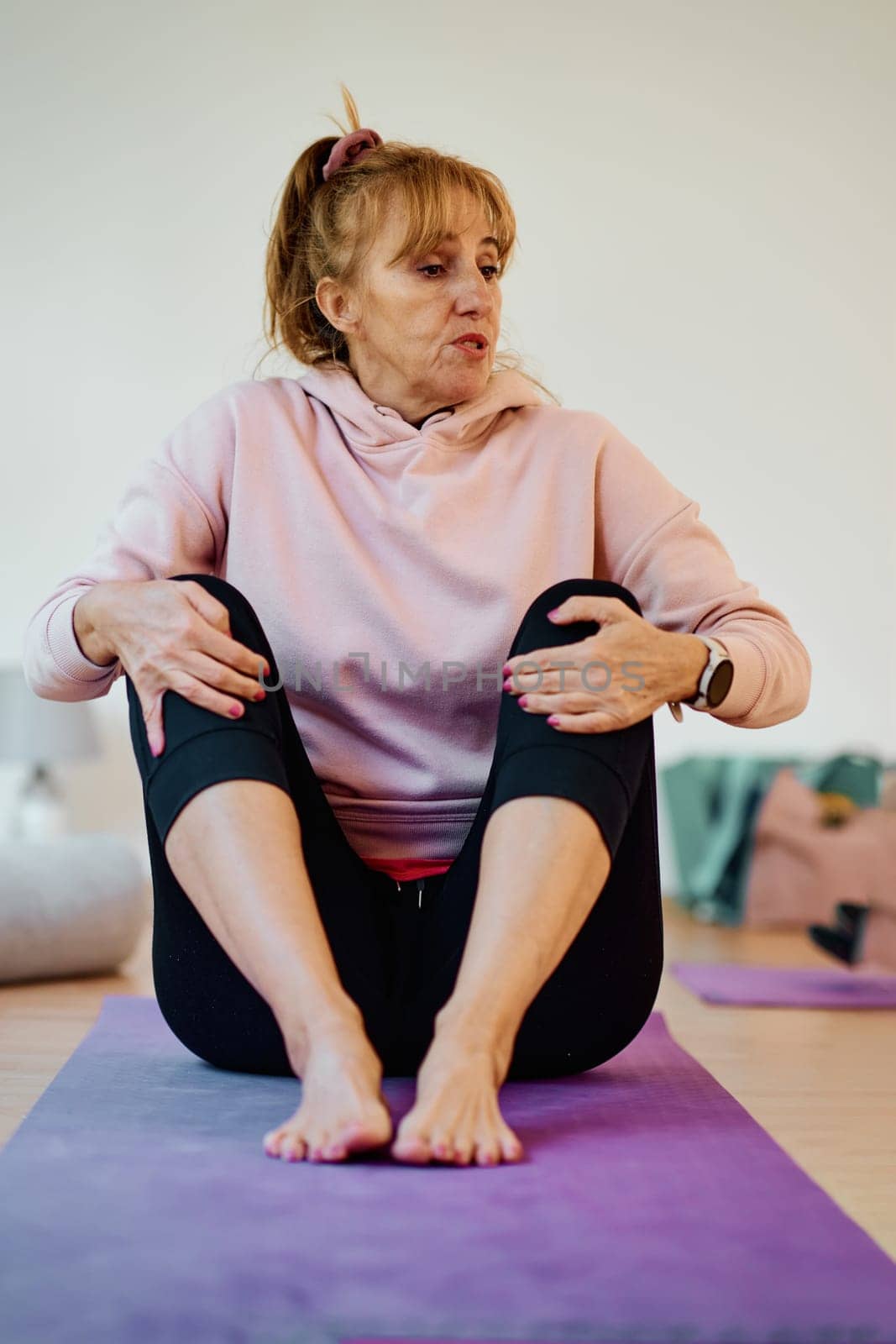 In a sunlit space, a senior woman gracefully practices rejuvenating yoga, focusing on neck, back, and leg stretches, embodying serenity and well-being by dotshock