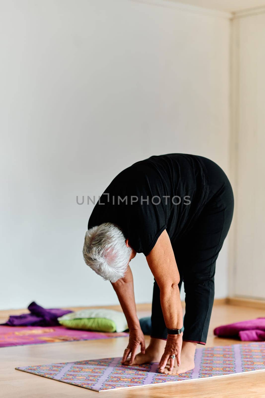 In a sunlit space, a senior woman gracefully practices rejuvenating yoga, focusing on neck, back, and leg stretches, embodying serenity and well-being.