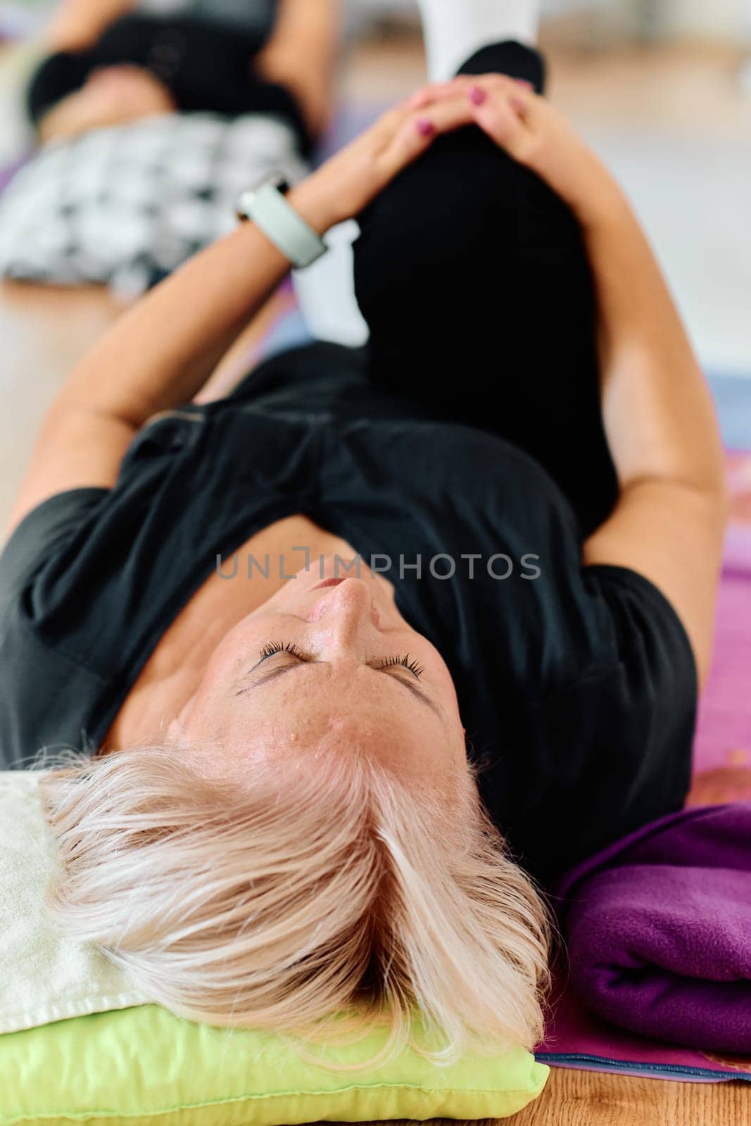 In a sunlit space, a senior woman gracefully practices rejuvenating yoga, focusing on neck, back, and leg stretches, embodying serenity and well-being by dotshock