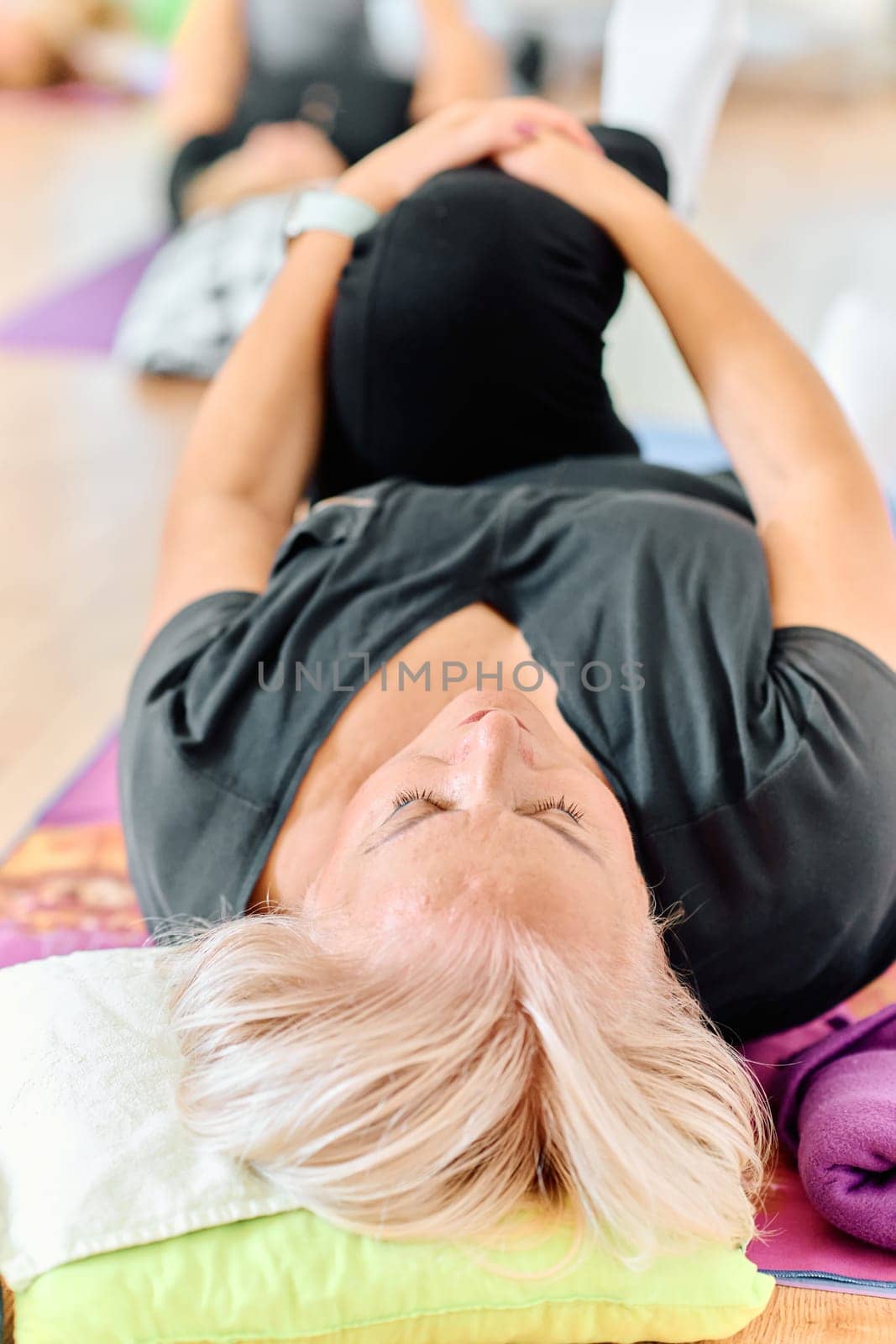 In a sunlit space, a senior woman gracefully practices rejuvenating yoga, focusing on neck, back, and leg stretches, embodying serenity and well-being.