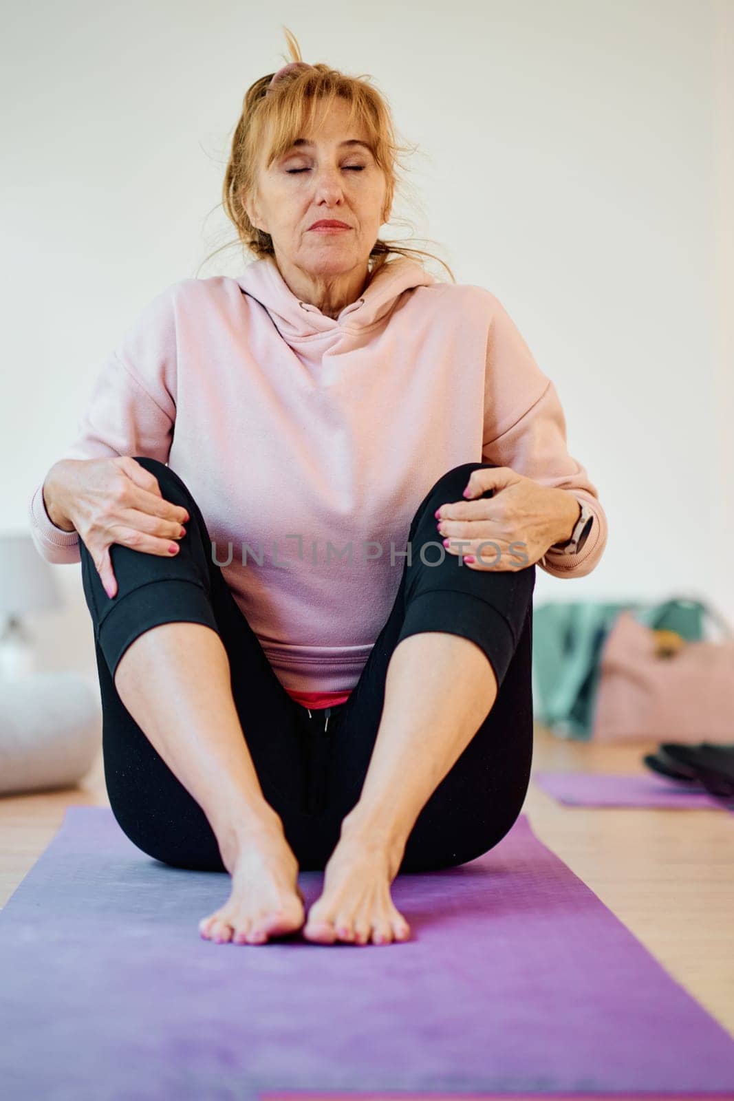 In a sunlit space, a senior woman gracefully practices rejuvenating yoga, focusing on neck, back, and leg stretches, embodying serenity and well-being.