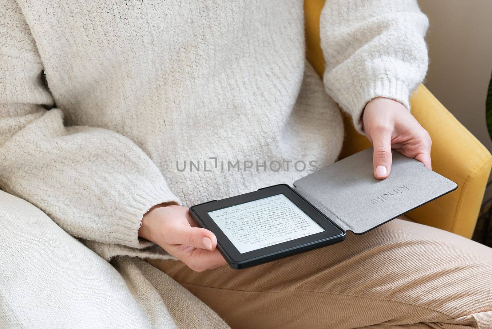 A man in a cozy sweater reads an ebook Kindle on a digital tablet, sitting comfortably. The setting is indoors and creates a warm and comfortable atmosphere