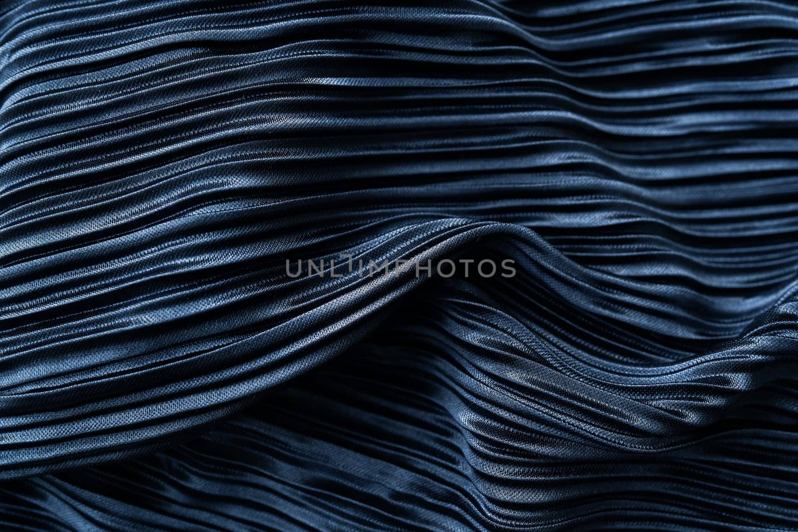 A dark blue pleated fabric with a shiny texture and intricate folds. It has an artistic feel due to the play of light and shadow on the folds