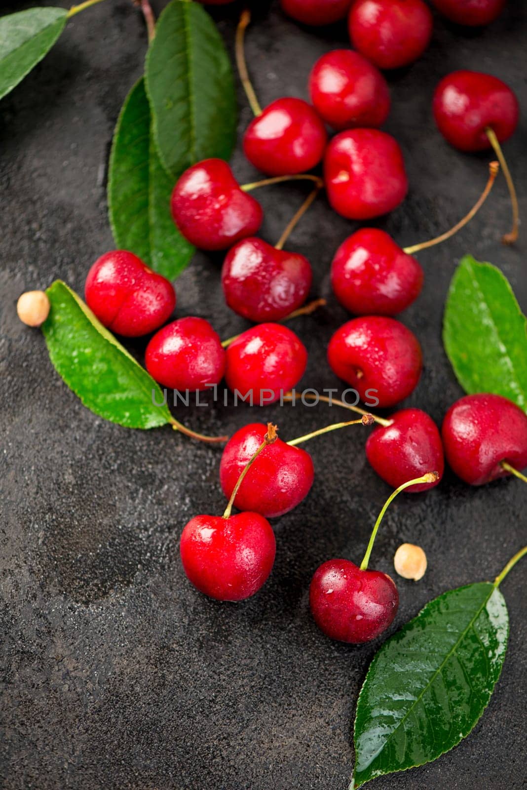 Ripe sweet cherry berry with leaves on a black wooden board. by aprilphoto
