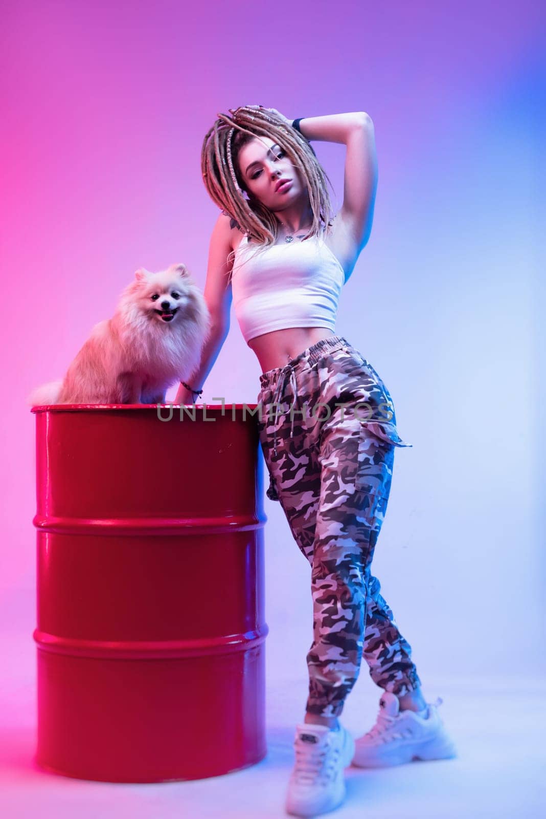 cool girl with braided dreadlocks on her head with a cute Pomeranian dog in neon light on a light background